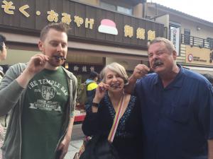 Matt is standing next to his parents. All three of them are biting into their own Fushimi Inari Sparrow on a stick. It does not look like a pleasant experience.